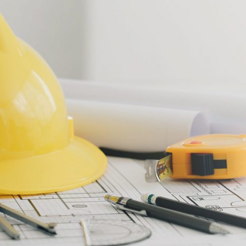 Yellow hard safety helmet hat and the blueprint, pen, ruler, protractor, and tape measure on the table at the construction site.for safety project of workman as engineer or worker, on concrete floor on city.banner white copy space.